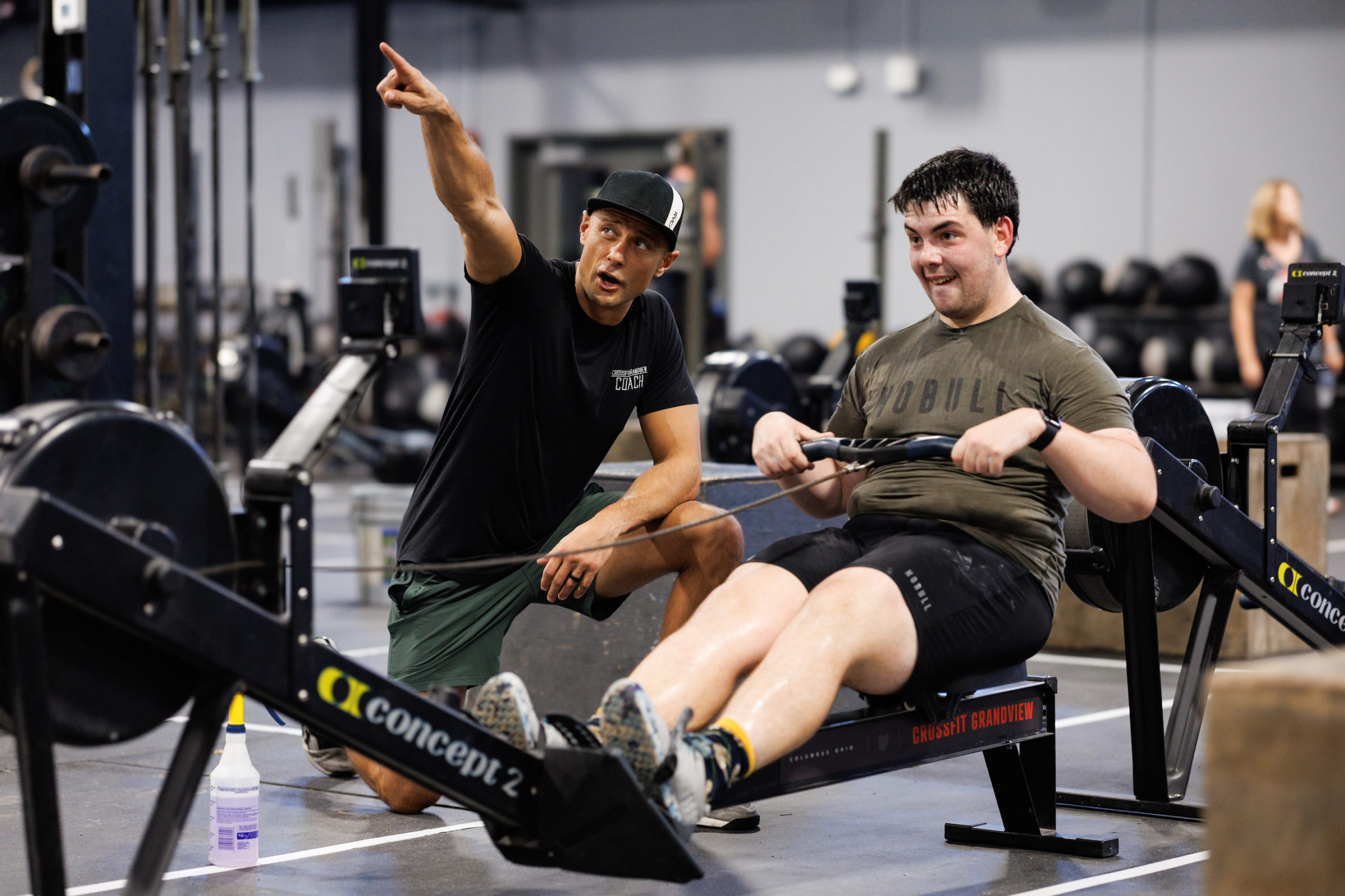 A trainer coaches an athlete on the rower. 