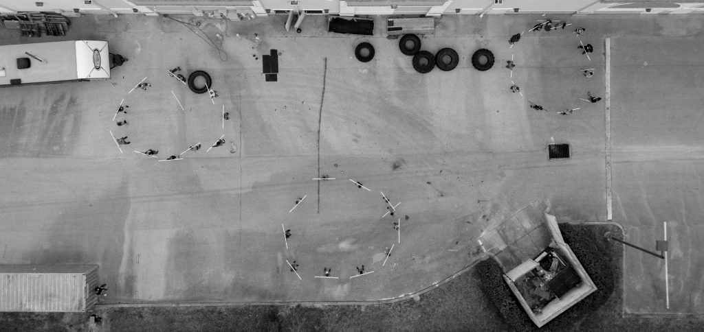 An overhead shot of circles of athletes practicing movement in a parking lot outside a CrossFit gym.