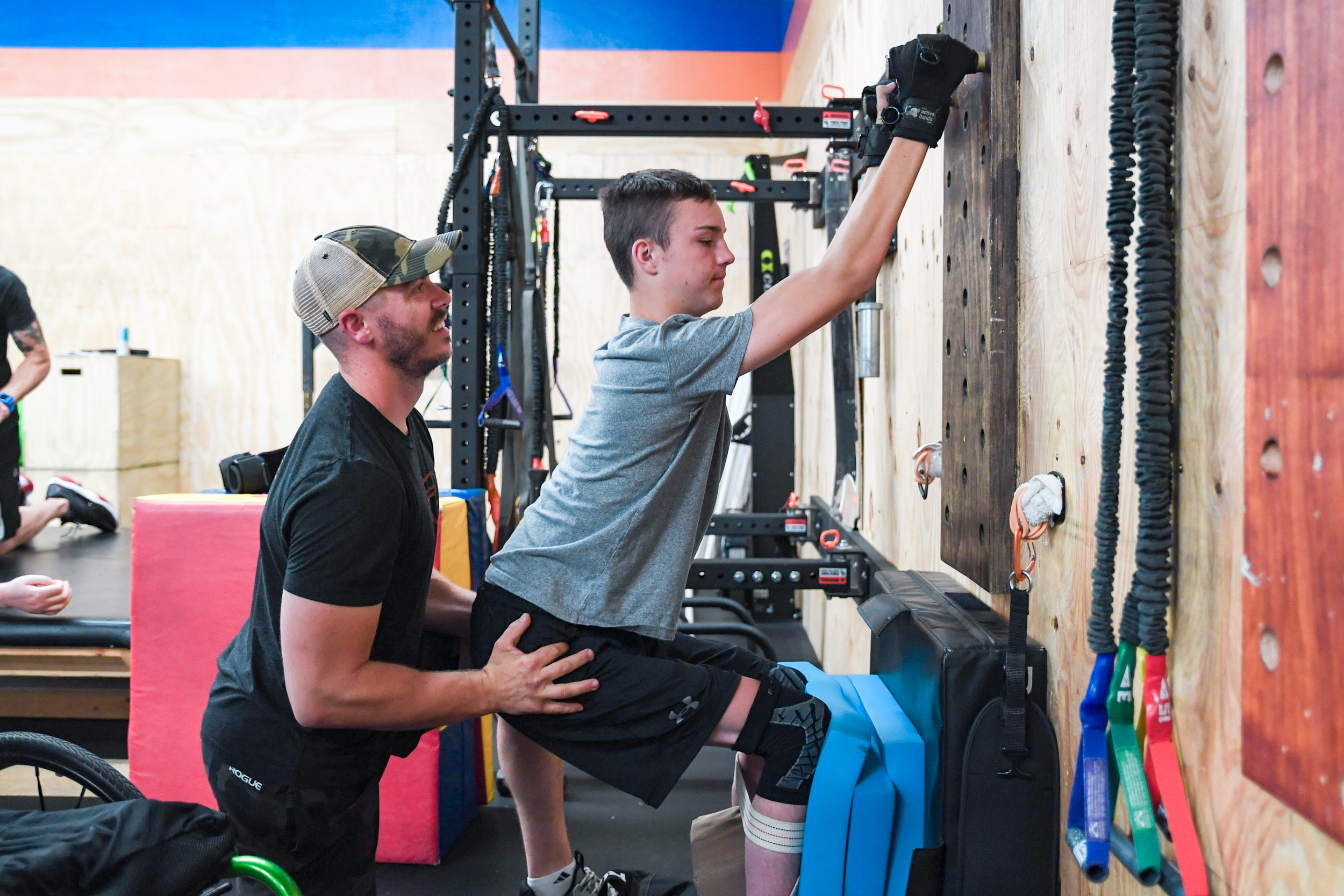 Raycer Frank performs squats and pegboard pull-ups assisted by his trainer.