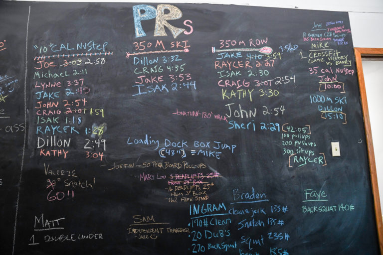 A chalkboard filled with athlete PRs.