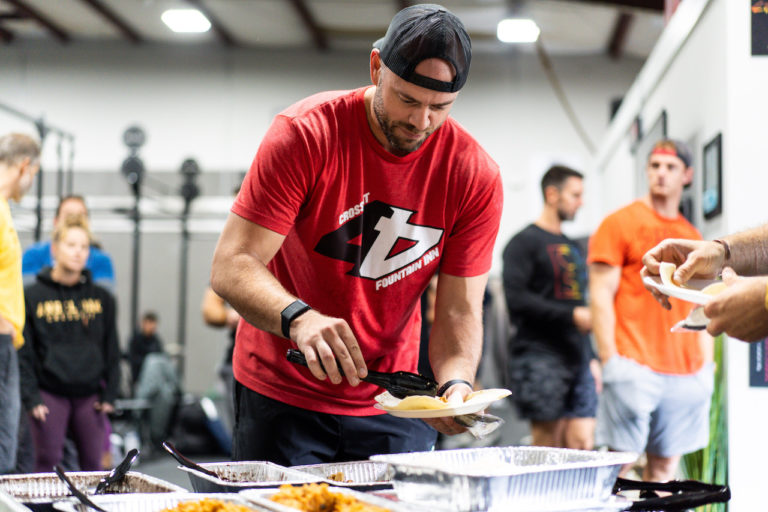 A man dishes food onto a plate in a CrossFit affiliate.