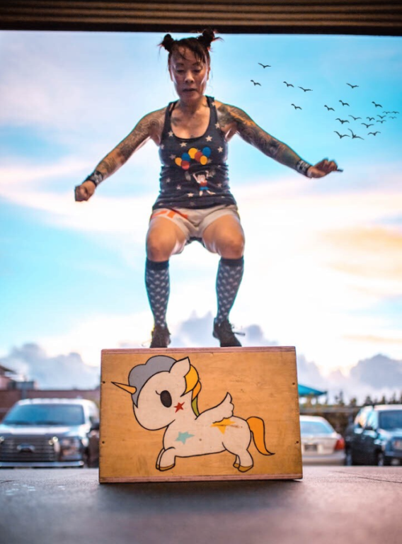 A woman jumps onto a box that's been painted with a unicorn.