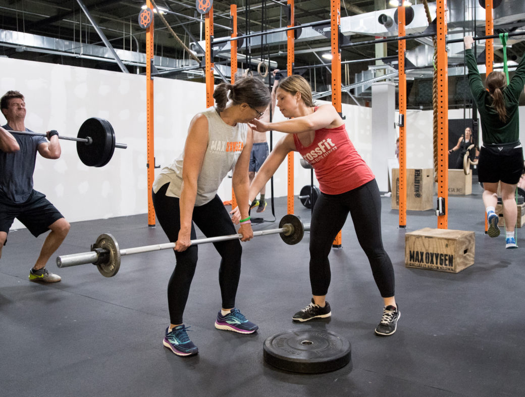 A CrossFit Seminar Staff Trainer positions an athlete holding a barbell.