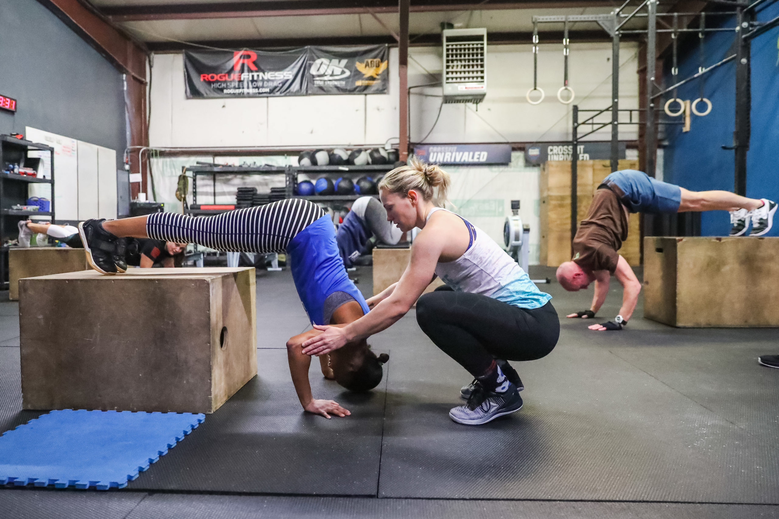 A coach works with an athlete on the box pike push-up.