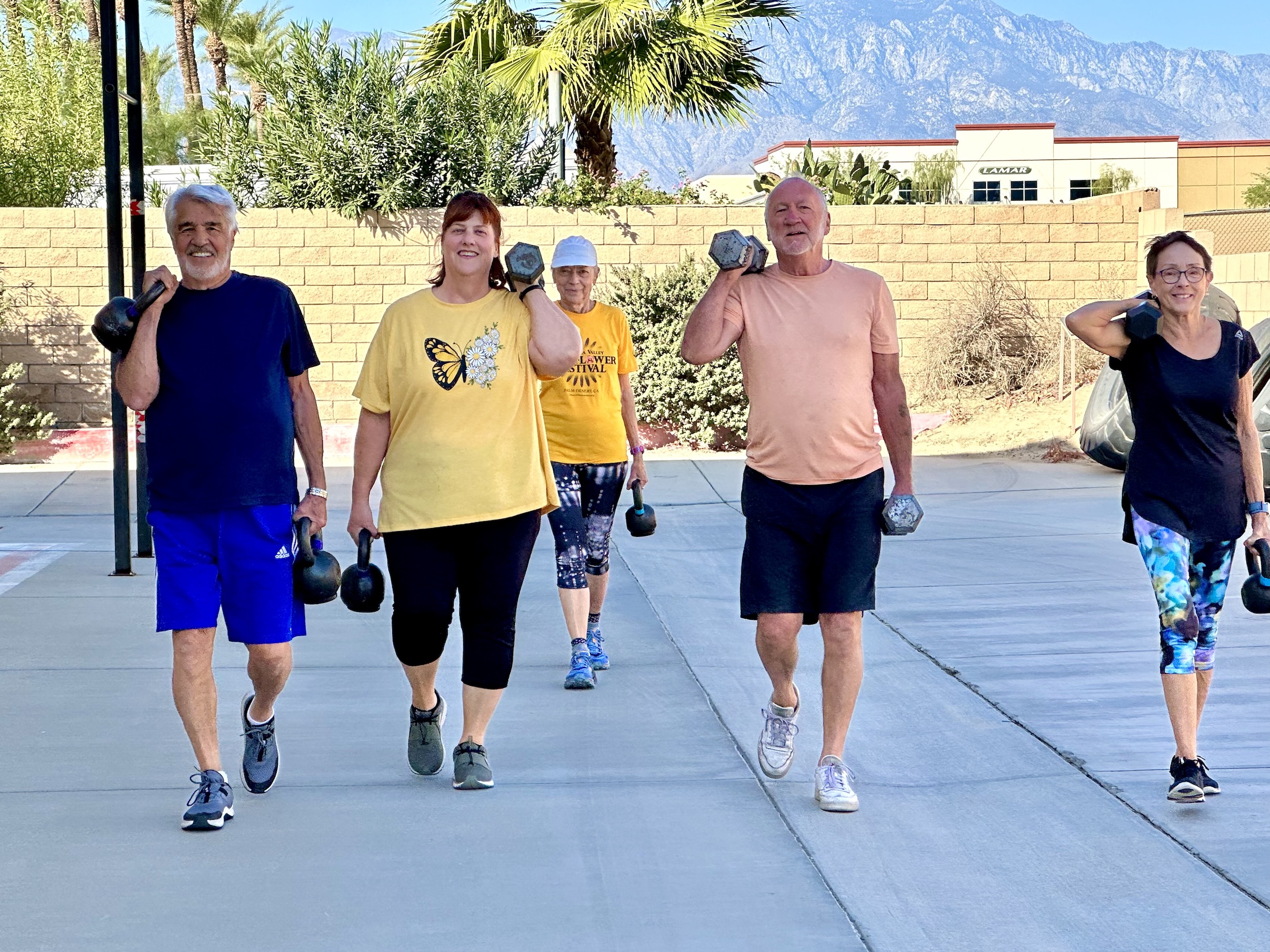 Senior athletes walk outside with dumbbells. 