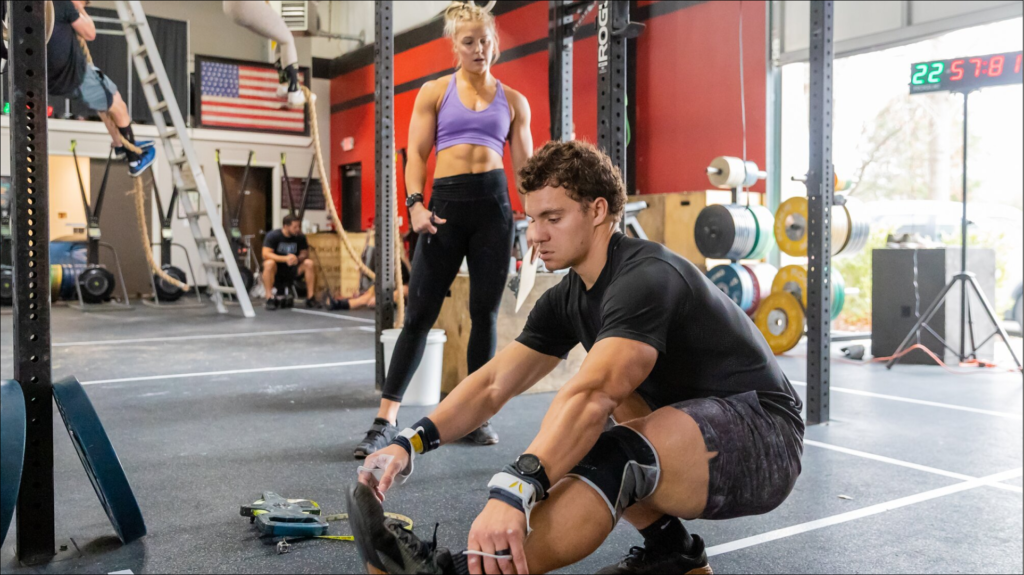 A muscular athlete executes a powerful clean and jerk with a barbell for a CrossFit Workout of the Day in a gym.